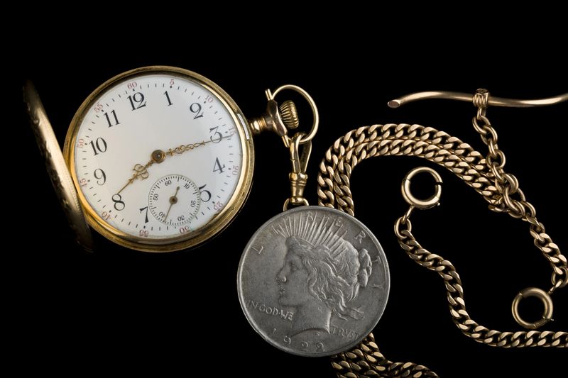 Gold pocket watch and chain beside a Peace dollar, the kind of gold Denver sellers bring to a private appointment